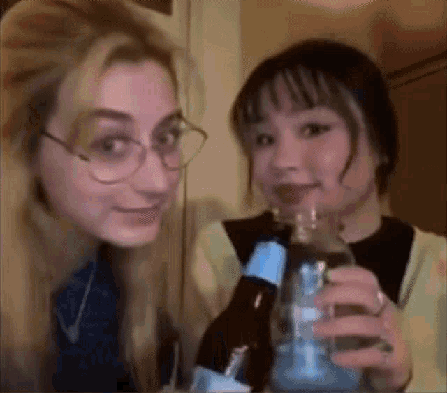 two young women are holding bottles of beer and drinking from them .