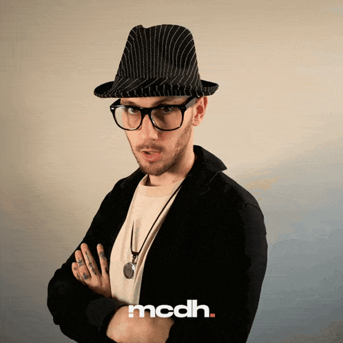 a man wearing a hat and glasses stands with his arms crossed in front of an ad for mcdh