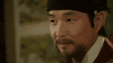 a man with a beard is wearing a hat and looking at something .