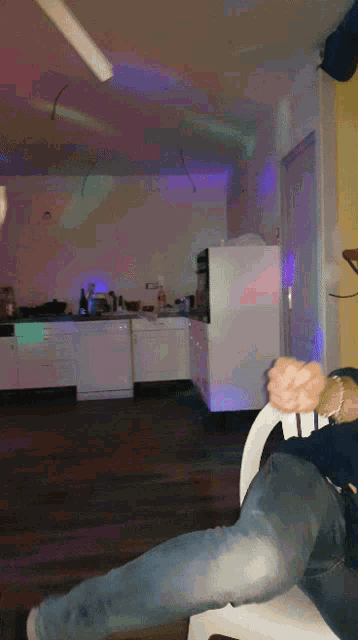 a person sitting on a chair in a kitchen with purple lights behind them