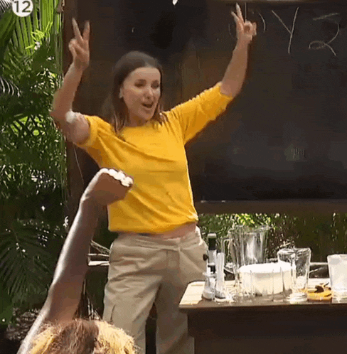 a woman in a yellow shirt is giving a peace sign while standing in front of a table .