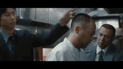 a group of men are standing next to each other in a kitchen and one of them is cutting another man 's hair .