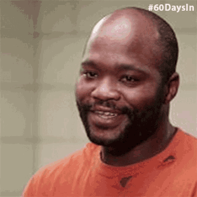 a bald man with a beard is smiling in a jail cell .