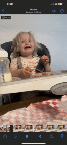 a baby in a high chair with a bottle in the background and the time of 8:02