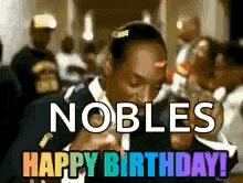 a man in a suit and tie is writing on a piece of paper with the words `` nobles happy birthday '' written on it .