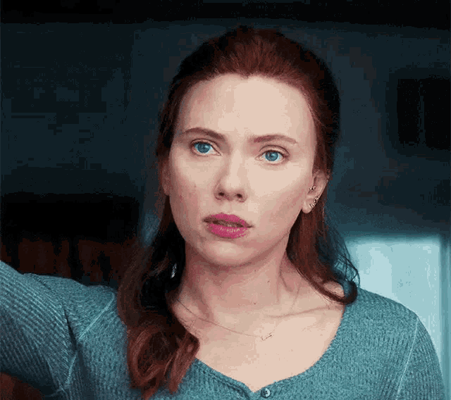 a close up of a woman 's face with red hair and blue eyes wearing a blue sweater .