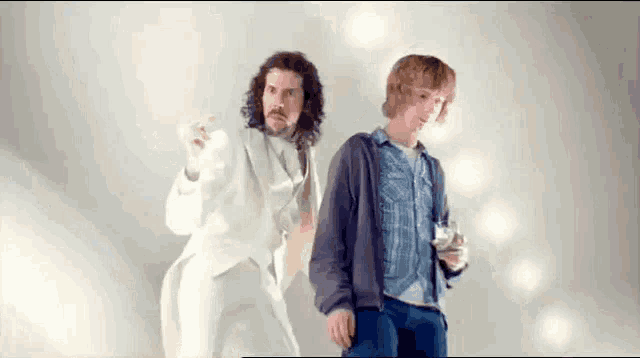 two men are standing next to each other in front of a white wall