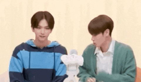 two young men are sitting next to each other and talking to each other while holding a stuffed animal .