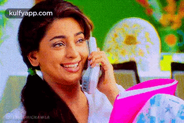 a woman is talking on a cell phone and smiling while holding a pink folder .