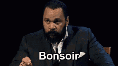 a man with a beard is wearing a suit and tie and making a funny face while talking .