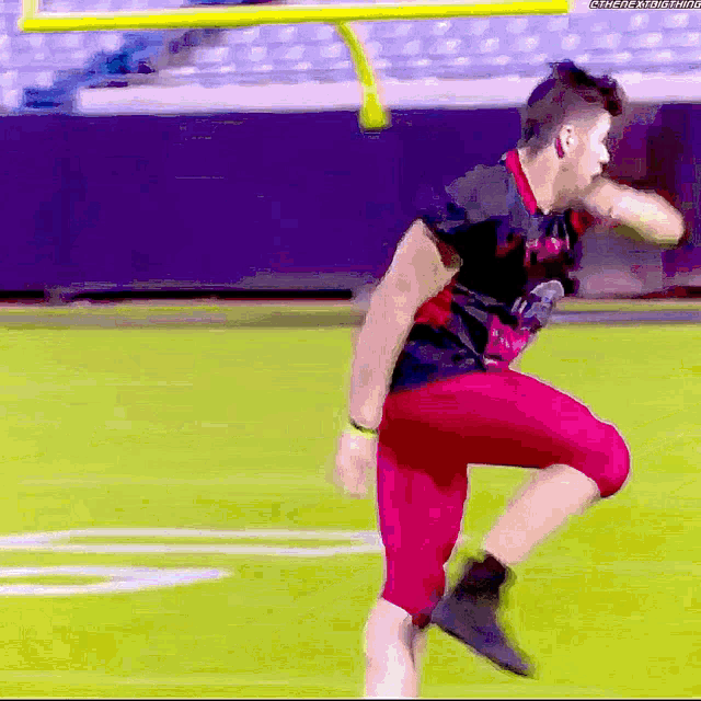 a football player in red shorts and a black shirt is running on the field .