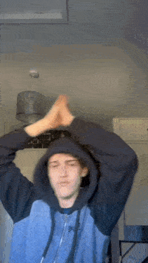 a young man wearing a hoodie and a beanie is clapping his hands in a room .