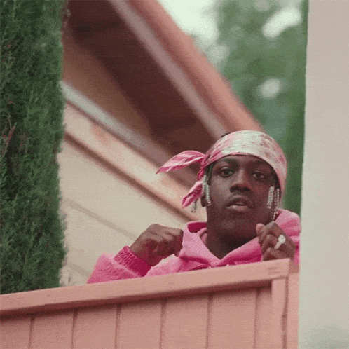 a man wearing a pink hoodie and a pink bandana looks out over a pink fence .