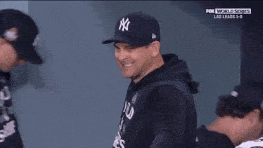 a man wearing a new york yankees hat smiles while talking to another man