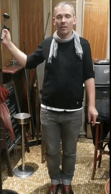 a man in a black sweater and gray jeans holds a hammer