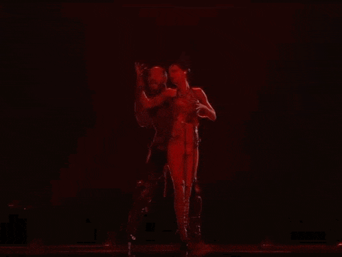a man and a woman are dancing on a stage in front of a microphone in a dark room .
