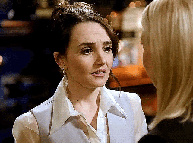 a woman in a white shirt and a grey vest talks to another woman