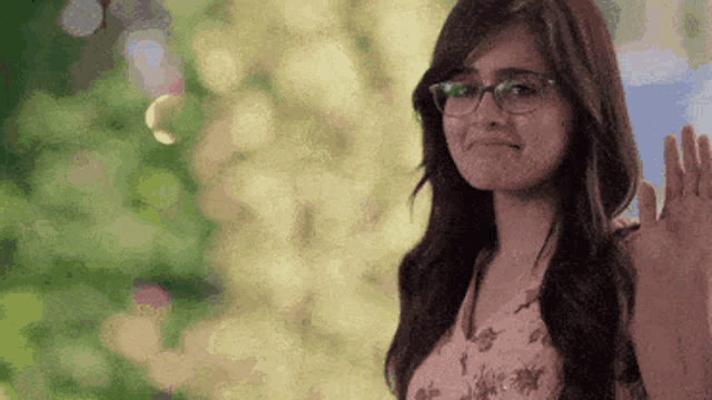 a woman wearing glasses is waving her hand and smiling