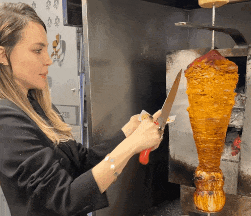 a woman is cutting a large piece of meat hanging from a skewer
