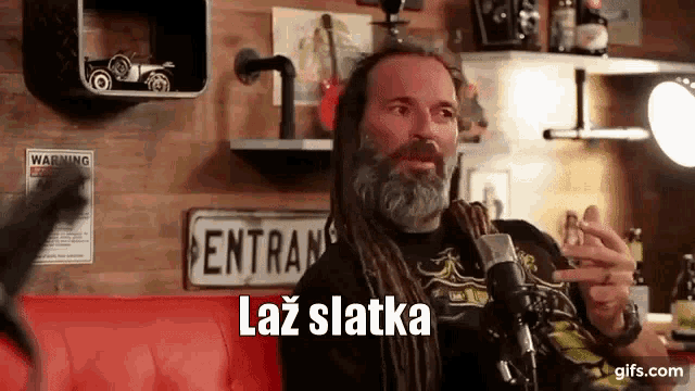 a man with dreadlocks and a beard is sitting in front of a microphone and talking into it .