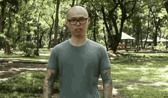 a man with glasses and tattoos is standing in a park