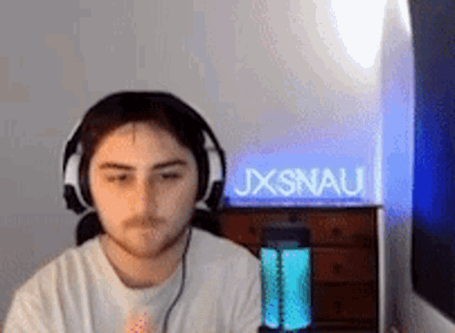 a young man wearing headphones is sitting in front of a sign that says jxsnau .