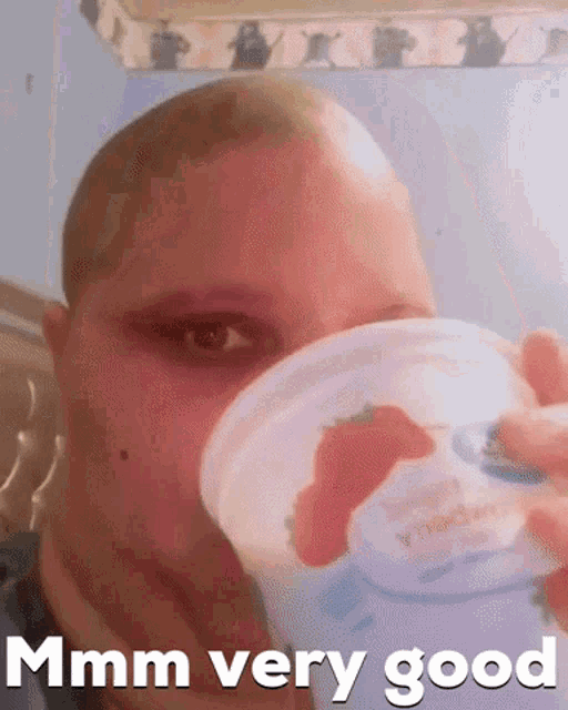 a woman with a shaved head is drinking a cup of yogurt with a strawberry in it