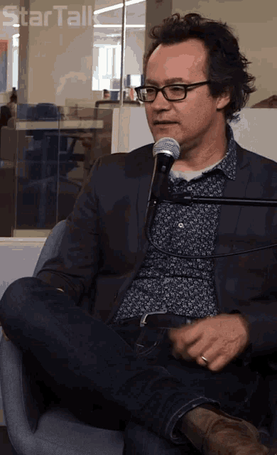 a man with glasses is sitting in front of a microphone with the words star talk below him