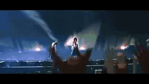 a woman singing on a stage with a man playing a guitar behind her