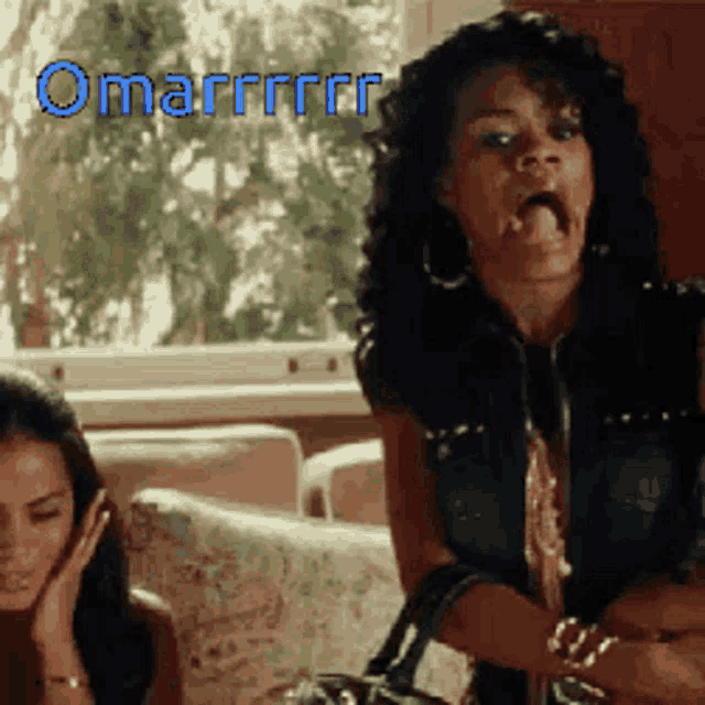 two women are sitting on a couch and one of them is making a funny face with the word omarrrr written in blue