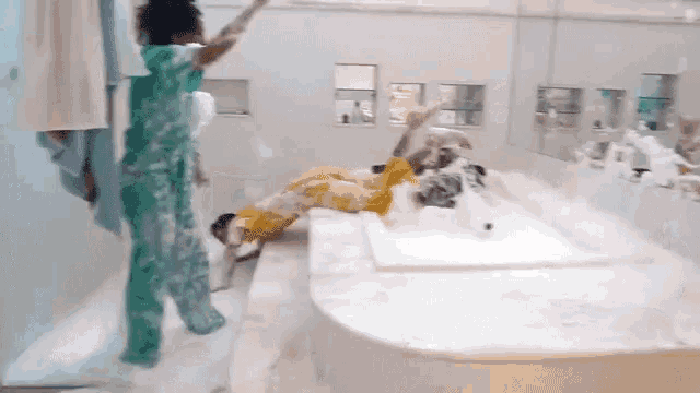 a woman in green pajamas is standing next to a woman in a yellow dress in a bathroom filled with foam