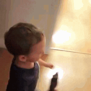 a young boy is holding a flashlight in his hand while standing in front of a mirror .