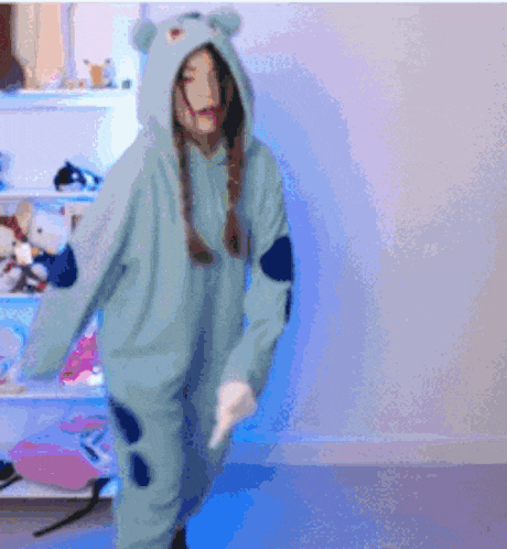 a girl in a blue bear costume is dancing in front of a shelf of stuffed animals