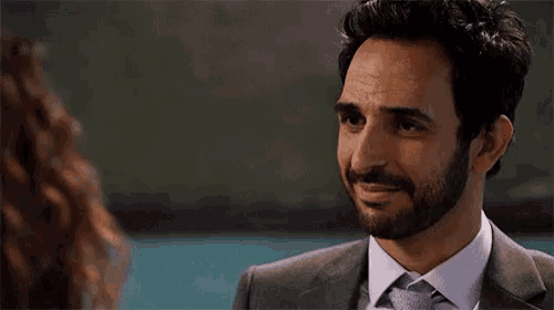 a man with a beard wearing a suit and tie smiles