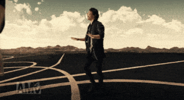 a man in a black jacket stands in the middle of a road with amv written on the bottom left