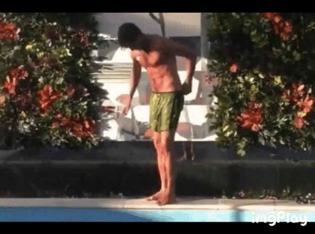 a shirtless man in green shorts is standing next to a pool