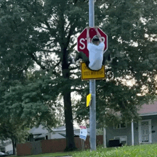 a man is hanging from a stop sign with a yellow sign below it that says does not stop