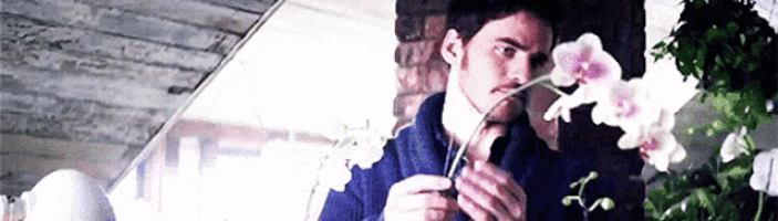 a man is holding a flower in his hand and smelling the flower .