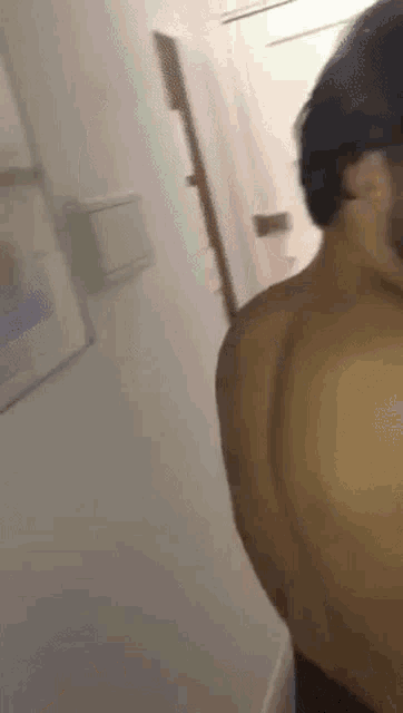 a man without a shirt is standing in a hallway with his back to the camera .