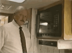 a man in a white shirt and tie is standing in front of a microwave that says ' cooking ' on it