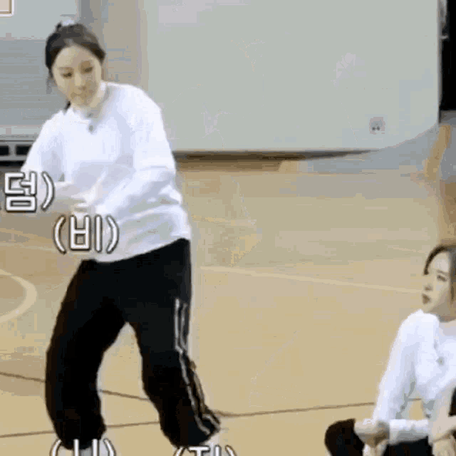 a woman in a white sweater and black pants is jumping in the air on a basketball court .