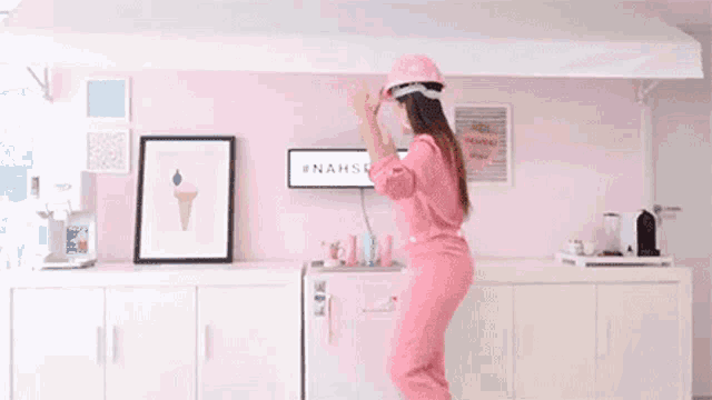 a woman in a pink jumpsuit is holding a picture frame in front of a sign that says nahspace