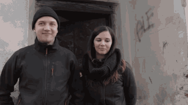 a man and a woman are standing in front of a wall that has the word ple written on it