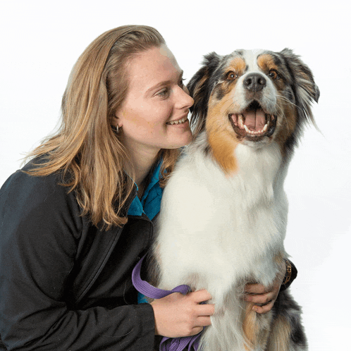 a woman in a black jacket is holding a brown and white dog
