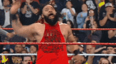 a wrestler in a red tank top is standing in a wrestling ring .