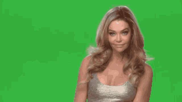 a woman in a silver tank top is smiling in front of a green screen