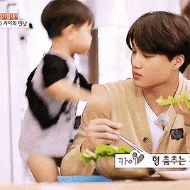 a man is eating lettuce with chopsticks while a little boy looks on ..