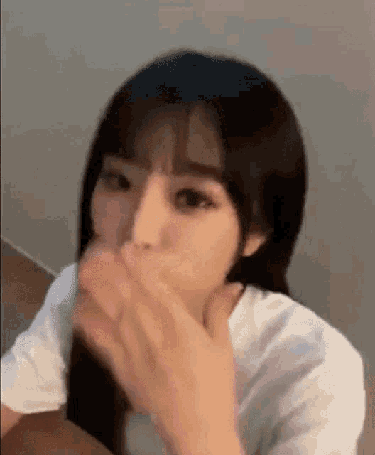 a woman with long black hair is covering her mouth with her hands .