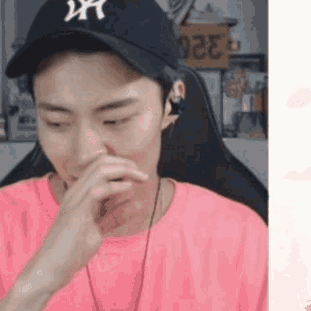 a man wearing a ny hat and a pink shirt is covering his mouth .