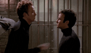 two men are standing next to each other in a jail cell and talking to each other .
